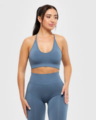 امرأة ترتدي حمالة صدر نسائية من BEST Define Seamless Racer Back باللون الأزرق الدخاني وبنطلون ضيق مزود بأشرطة متقاطعة من الخلف.