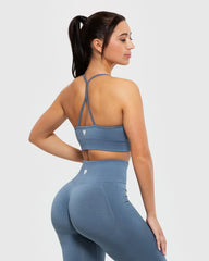 ترتدي المرأة حمالة صدر BEST Define Seamless Racer Back للنساء باللون الأزرق الدخاني، وسروالًا ضيقًا مع تفاصيل متقاطعة على الظهر.