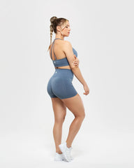 امرأة ترتدي شورتًا أزرق اللون من BEST Define Scrunch بدون خياطة | يقف Smoke Blue أمام خلفية بيضاء.