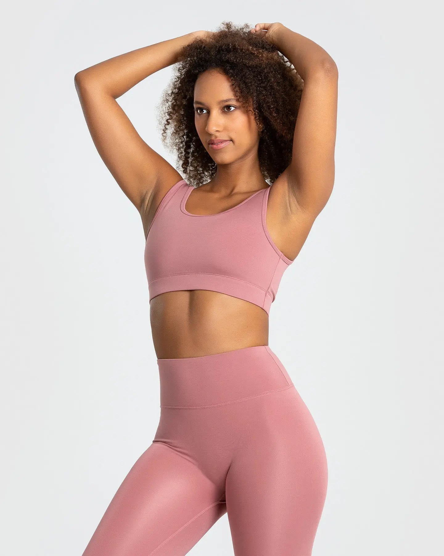 العارضة ترتدي صدرية رياضية "Essential Sports Bra" وردي فاتح من "WOMEN'S BEST" وبنطال ضيق.