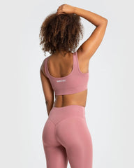 تبدو الواجهة الأمامية لامرأة ترتدي حمالة صدر رياضية Essential Sports Bra بلون Dusty Pink وبنطال ضيق من WOMEN'S BEST.