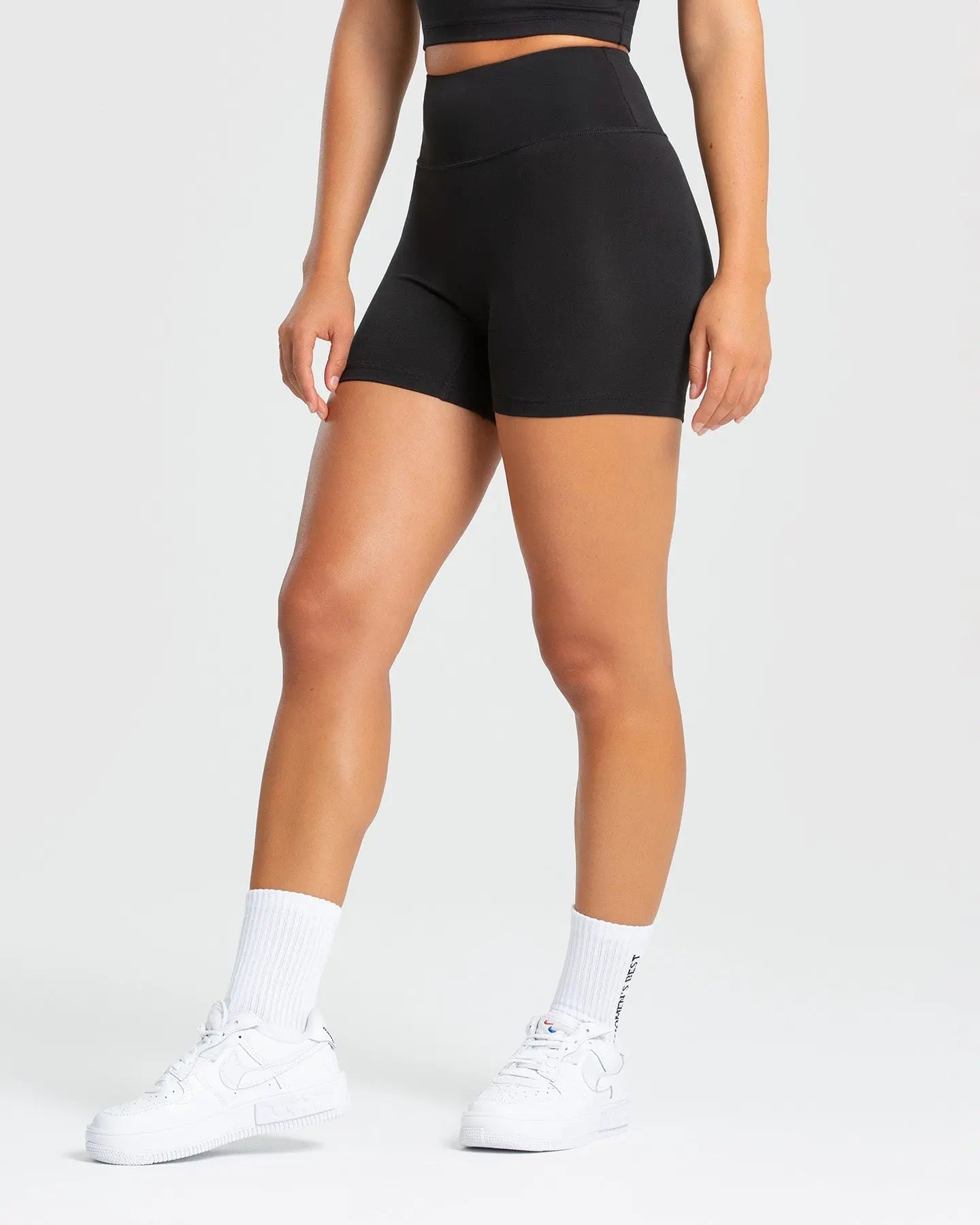 الوصف: امرأة ترتدي شورتًا أسودًا من Essential Shorts من WOMEN'S BEST وقميصًا أبيض.