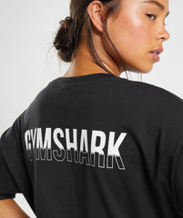 امرأة ترتدي تي شيرت أسود بجزء كبير الحجم من Gymshark | United We Sweat، ينضح بالراحة والأناقة.