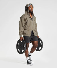 رجل يرتدي Gymshark | سترة بغطاء للرأس بسحاب من United We Sweat Power تحمل قضيبًا مما يوفر الراحة والأناقة.