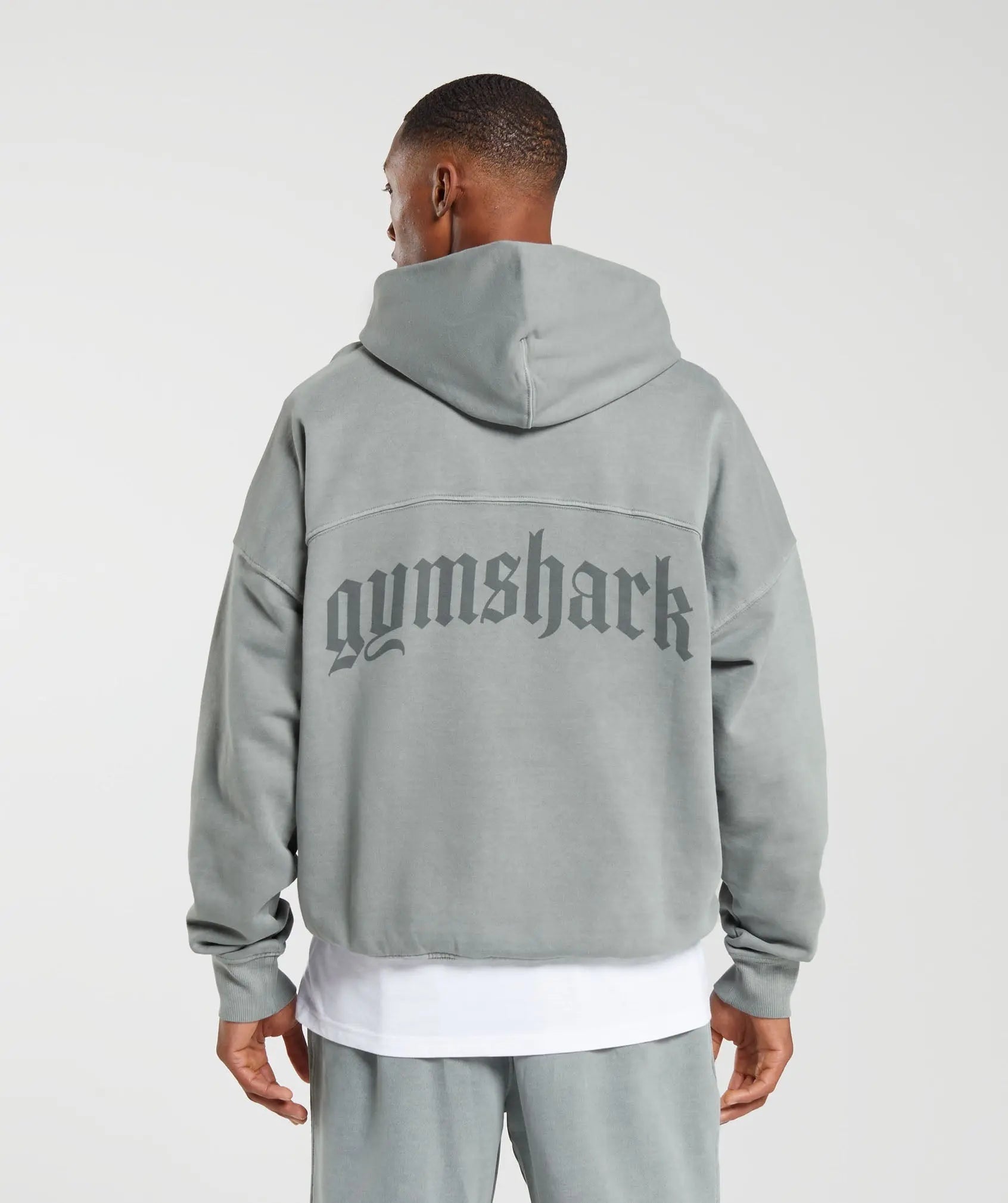 رجل يرتدي هوديي رمادي ثقيل الوزن من تصميم كلاسيكو مع كلمة Gymshark | يونايتد نحن نتعرق عليه.
