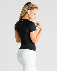 المنظر الخلفي لامرأة ترتدي بنطالًا ضيقًا أبيض اللون وقميصًا أسود اللون من ماركة Power Seamless الأفضل للنساء.