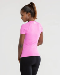 المنظر الخلفي لامرأة ترتدي تي شيرت BEST Power Seamless للسيدات باللون الوردي الفلوكس وبنطال ضيق أسود أثناء ممارسة التمارين.