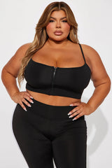امرأة ذات حجم كبير ترتدي حمالة صدر رياضية سوداء من تصميم Break A Sweat Active من Fashion Nova، وقميص قصير بسحاب، وطماق بيضاء.