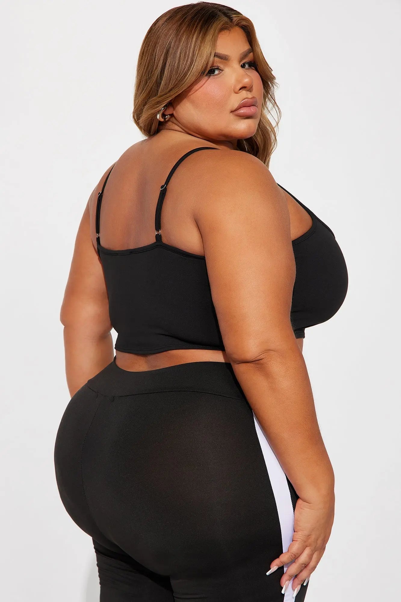 امرأة نشطة ذات حجم كبير ترتدي حمالة الصدر الرياضية Break A Sweat Active باللون الأسود من Fashion Nova، إلى جانب السراويل الضيقة البيضاء.