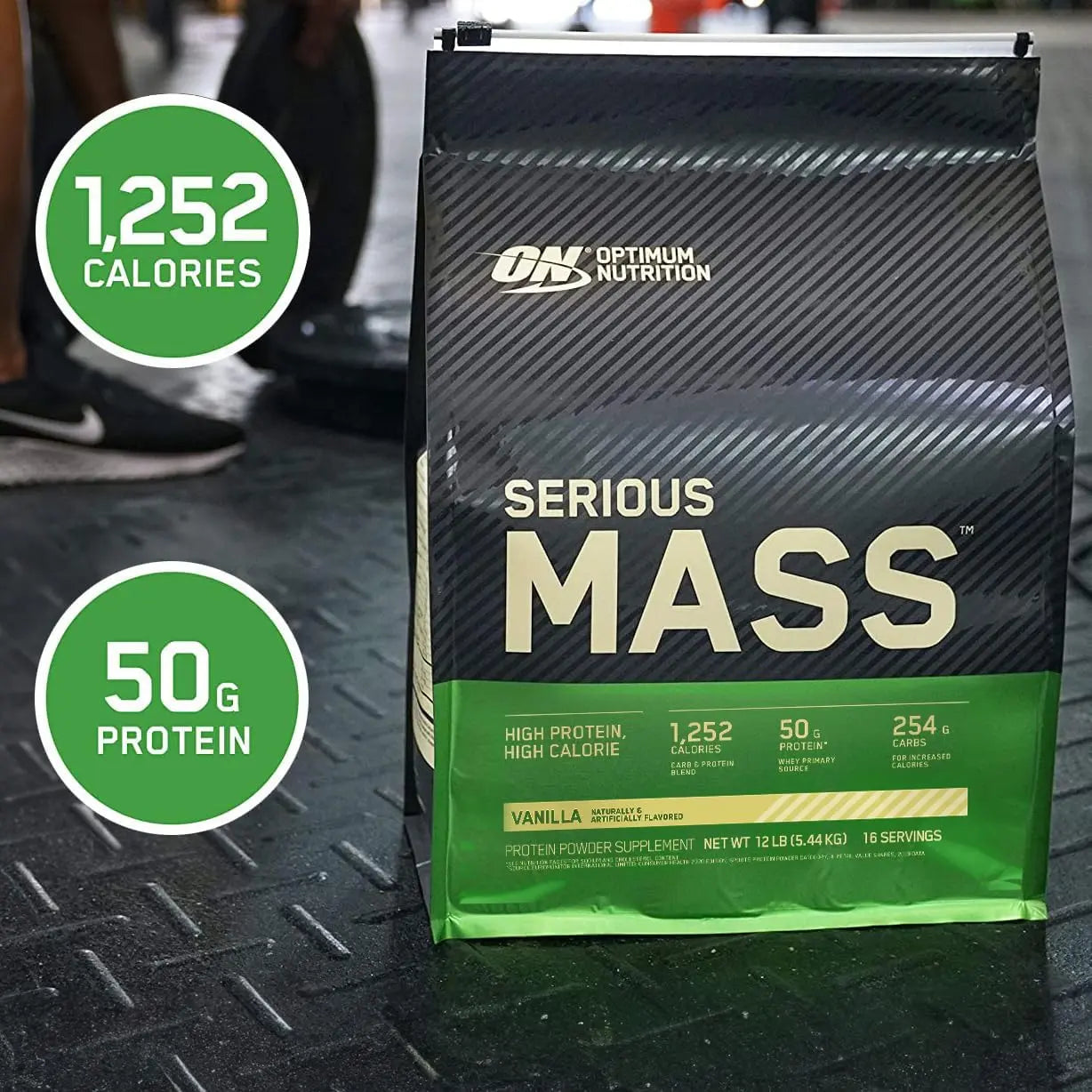 يتم وضع كيس بروتين سعودي شارك سيريوس ماس من شركة أوبتيموم نيوتريشن (ON) بشكل ملائم على أرضية صالة الألعاب الرياضية، مما يوفر حلاً فعالاً لزيادة الوزن وتنمية العضلات.