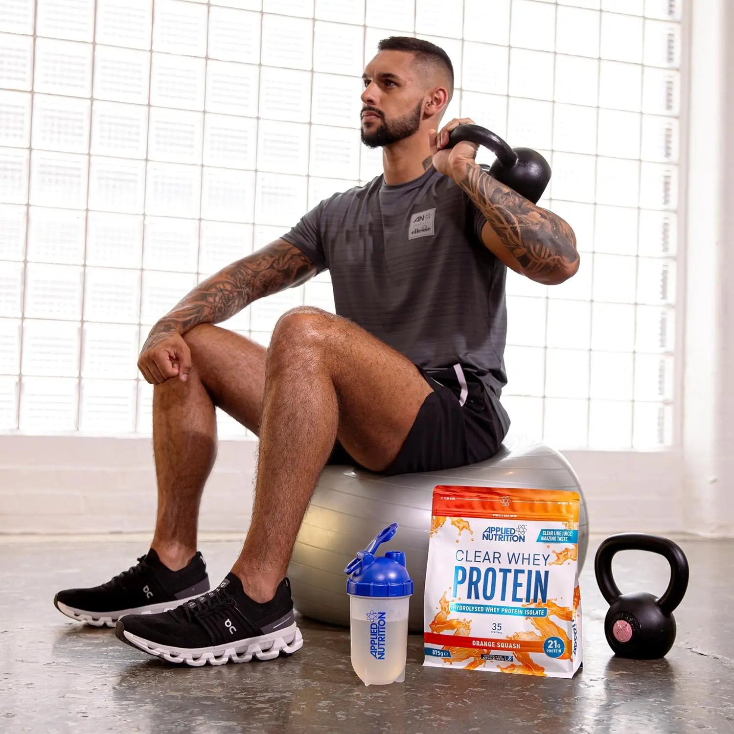 رجل يجلس على كرة يحمل جرسًا وتغذية تطبيقية من SAUDI SHARK's Clear Whey Isolate - بروتين مصل اللبن المعزول، مسحوق منعش عالي البروتين، نكهات على طراز عصير الفاكهة (البطيخ) (875 جم - 35 حصة).
