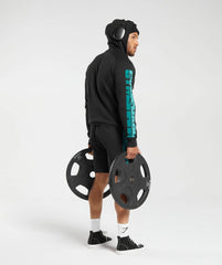 تفاصيل: رجل يرتدي هودي "Bold Hoodie" أسود ويحمل شريط "United We Sweat" للجمباز من "Gymshark".