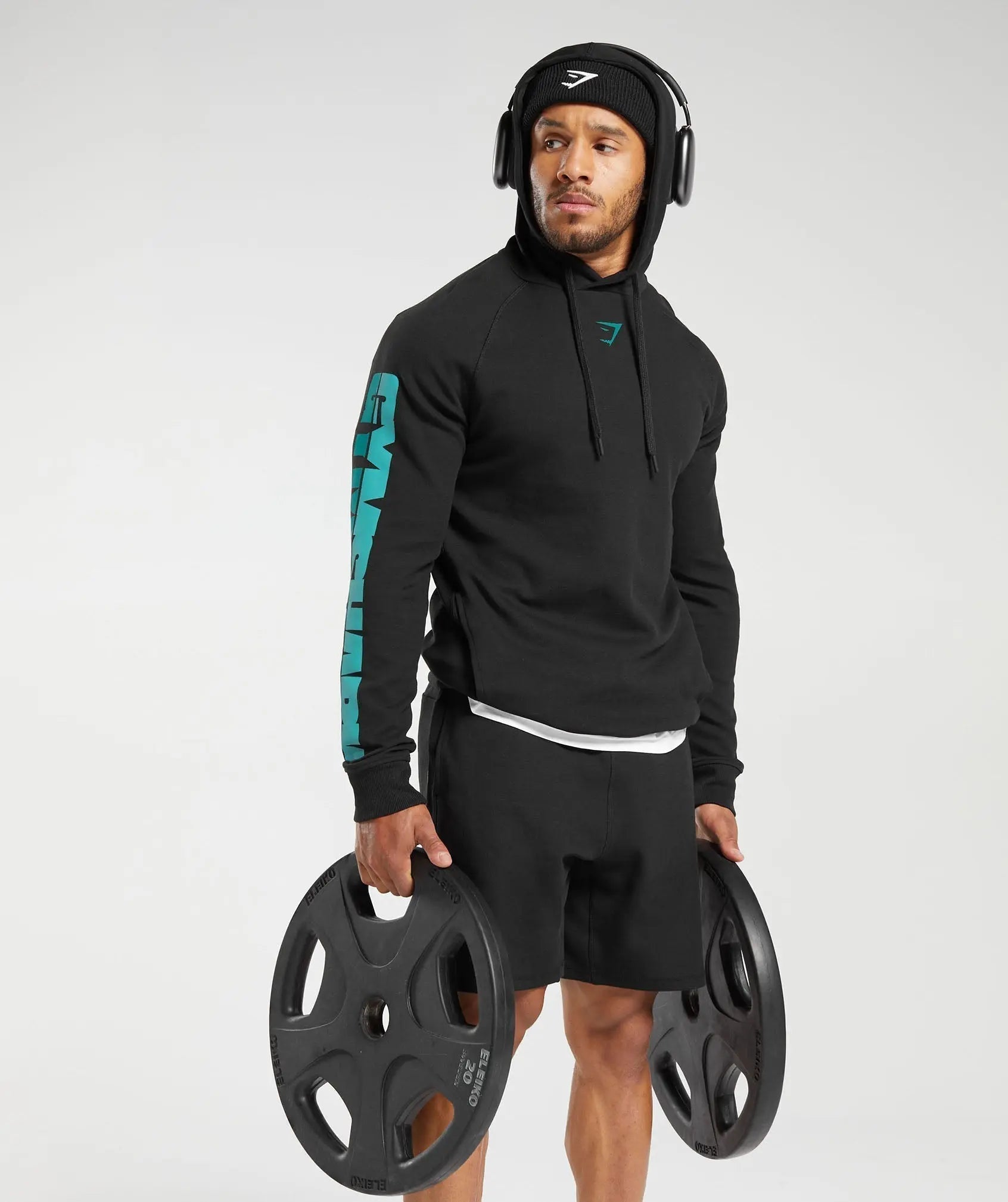 رجل يرتدي Gymshark | سترة بغطاء رأس جريئة من United We Sweat تحمل زوجًا من الأوزان مصنوعة من مواد عالية الجودة.