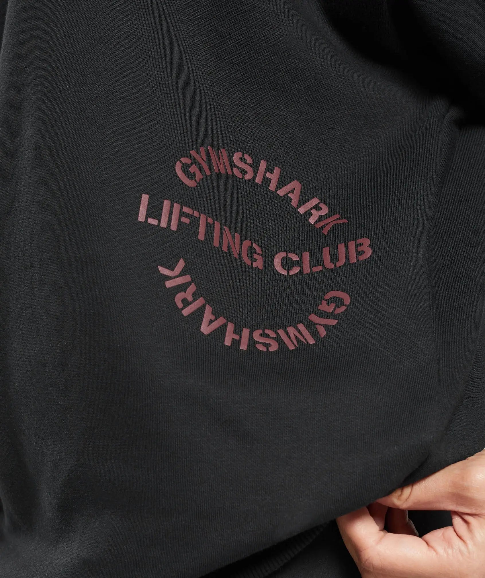وصف: امرأة ترتدي كنزة "Built Oversize Sweatshirt" بنقشة مكبرة تحمل كلمات قصة "United We Sweat" من Gymshark.