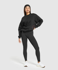 وصف: امرأة ترتدي كنزة "Built Oversize Sweatshirt" من "Gymshark | United We Sweat" وبنطال قصير.