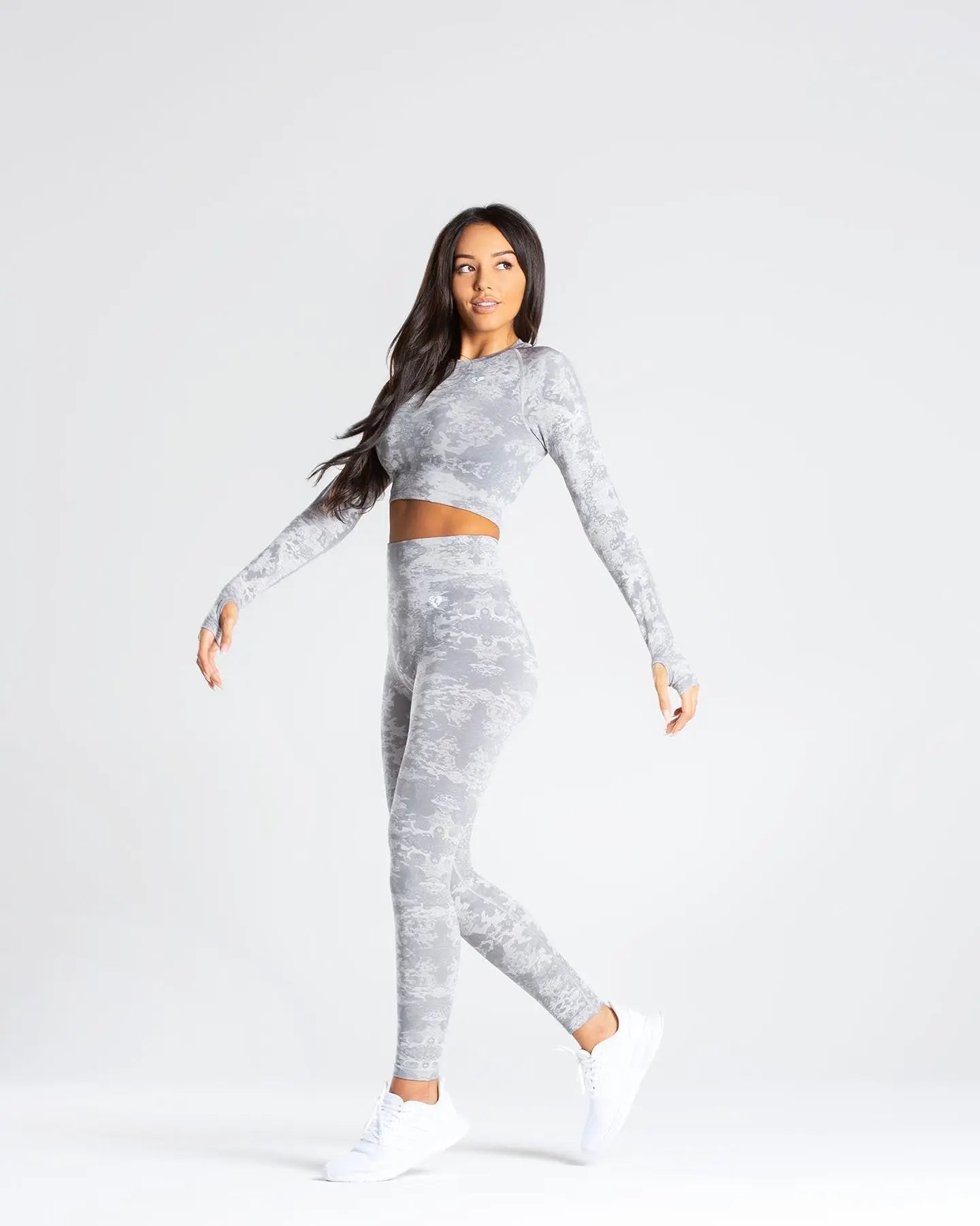 امرأة ترتدي قميص WOMEN'S BEST Camo Seamless قصير الأكمام باللون الرمادي مصنوع من قماش بدون خياطة وحذاء رياضي أبيض.