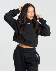 وصف: سيدة ترتدي كنزة قلنسوة "Comfort Cropped Hoodie" قصيرة وبنطال رياضي