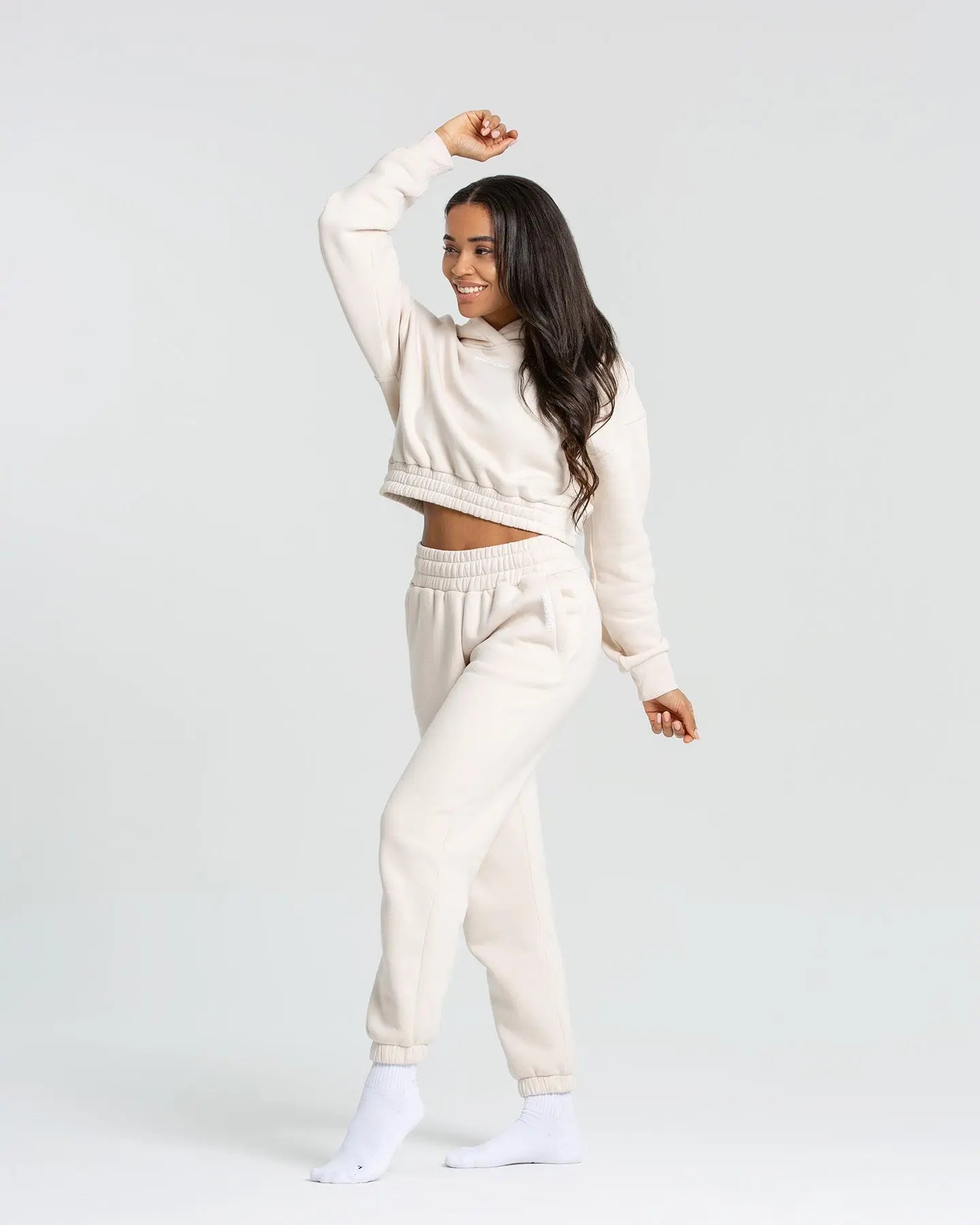 النموذج يرتدي كنزة "Comfort Cropped Hoodie | Sand" من WOMEN'S BEST وسروال رياضي أبيض.