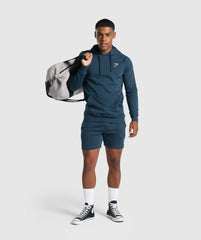 رجل يرتدي Gymshark | سترة بغطاء للرأس وسروال قصير من United We Sweat Crest يحمل حقيبة من القماش الخشن.