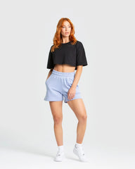 وصف: امرأة ترتدي قميص "Comfort Oversize Cropped Short Sleeve T-shirt" أسود من WOMEN'S BEST وبنطال أزرق.