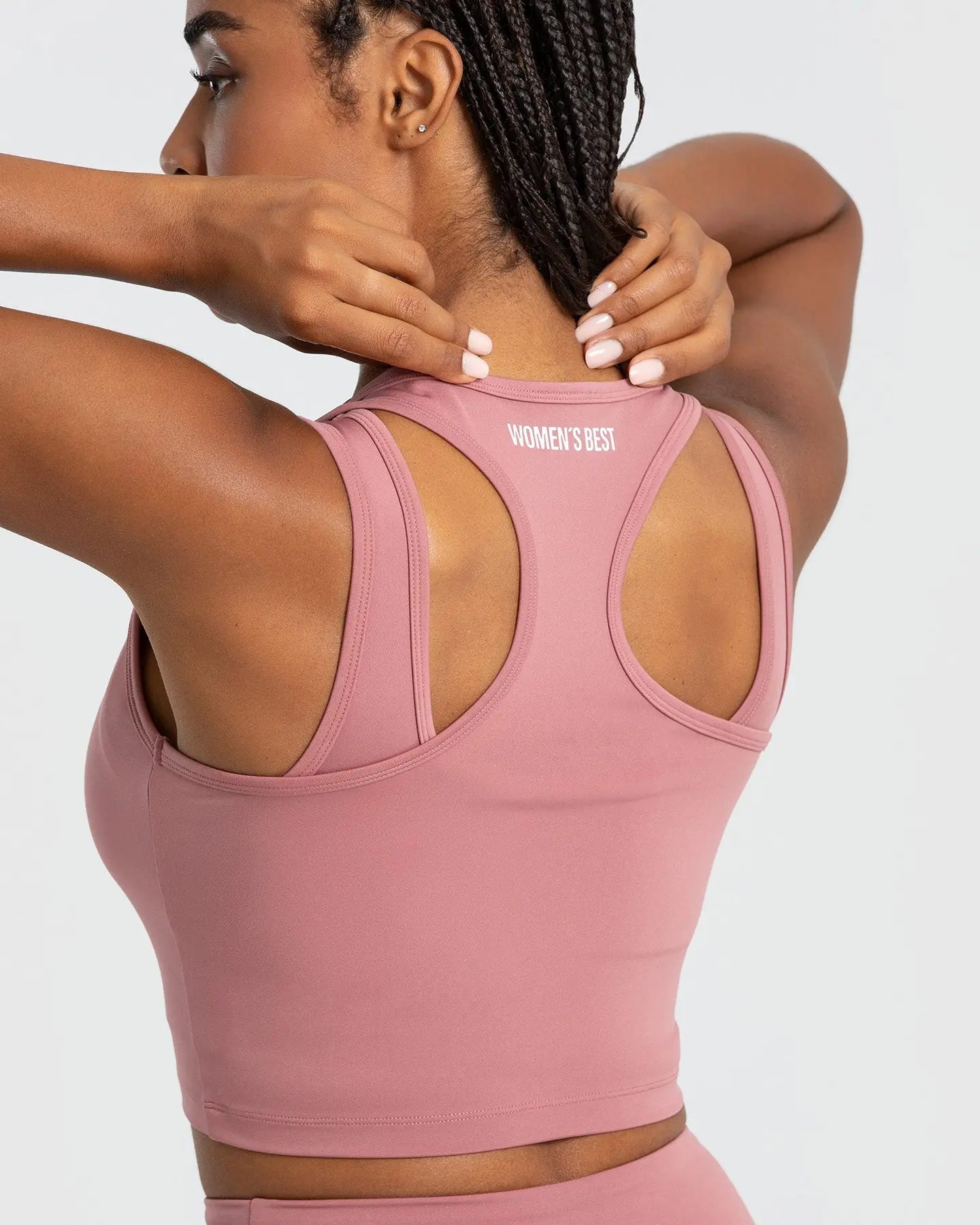 ملابس داخلية لامرأة ترتدي قميص WOMEN'S BEST Essential Crop Tank Top بلا أكمام بلون وردي فاتح.
