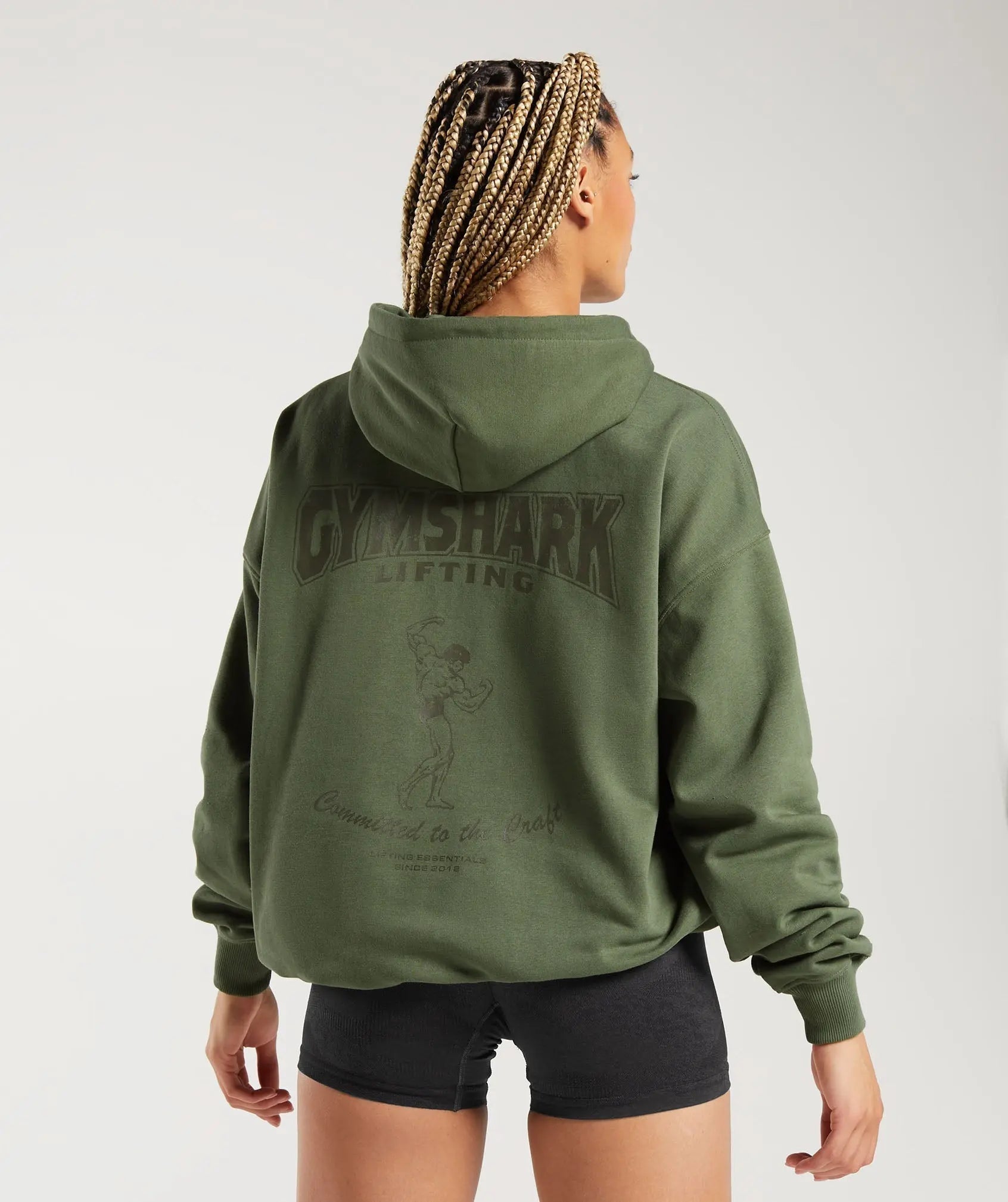 وصف: امرأة ترتدي كنزة بغطاء رأس Commident To The Craft Hoodie ذات كلمات Gymshark عليها.