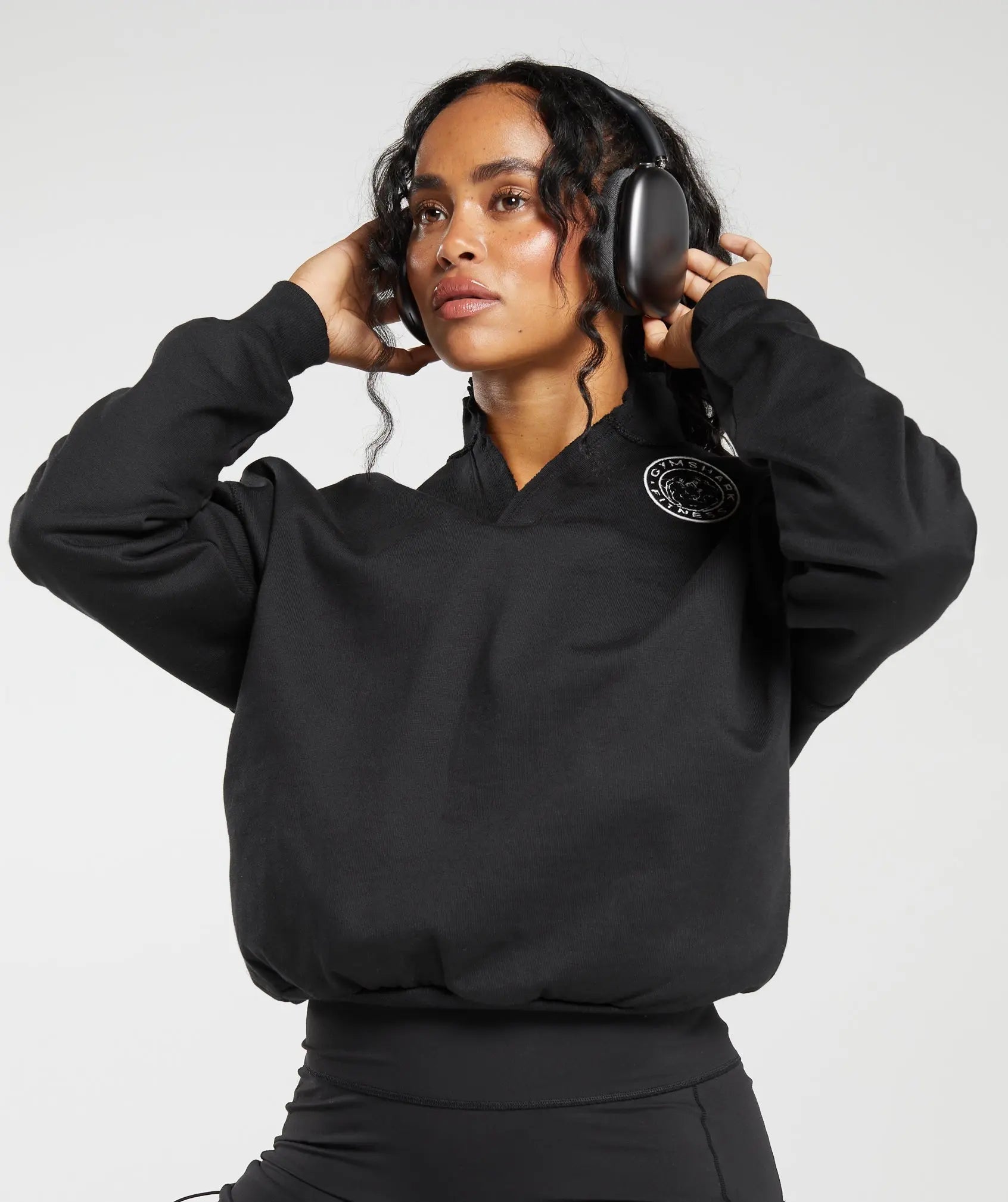 وصف: امرأة ترتدي قميصًا أسود من "Gymshark | United We Sweat" من طراز "Legacy Oversize Sweatshirt".