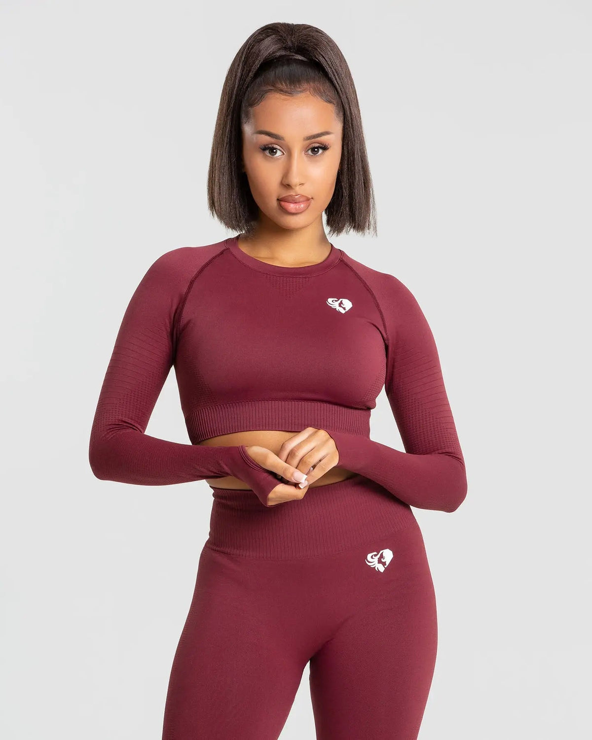 وصف: امرأة ترتدي هي بلوزة "Power Seamless Long Sleeve Crop Top | Burgundy" من WOMEN'S BEST، مصنوعة من قماش مرن بالفعل مكسور.