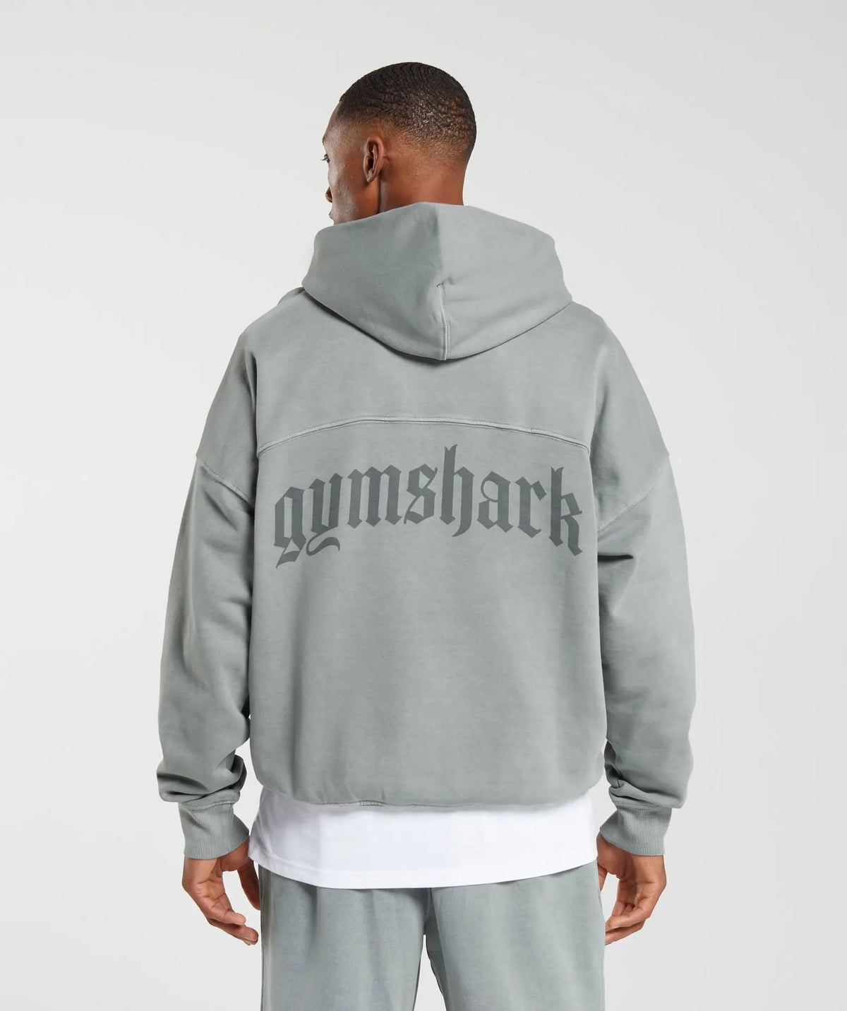 رجل يرتدي هوديي رمادي ثقيل الوزن من تصميم كلاسيكو مع كلمة Gymshark | يونايتد نحن نتعرق عليه.