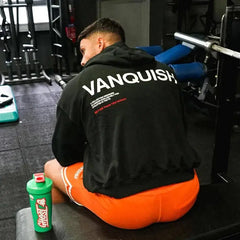 رجل يجلس على مقعد في صالة الألعاب الرياضية ويرتدي باور أب | سترة Power Up Vanquish ذات القلنسوة، تجسّد جوهر أسلوب القرش السعودي.