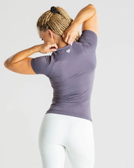 الجزء الخلفي لامرأة ترتدي طماقًا بيضاء وتي شيرت Power Seamless باللون الرمادي | فحم، عرض راحة ومرونة.